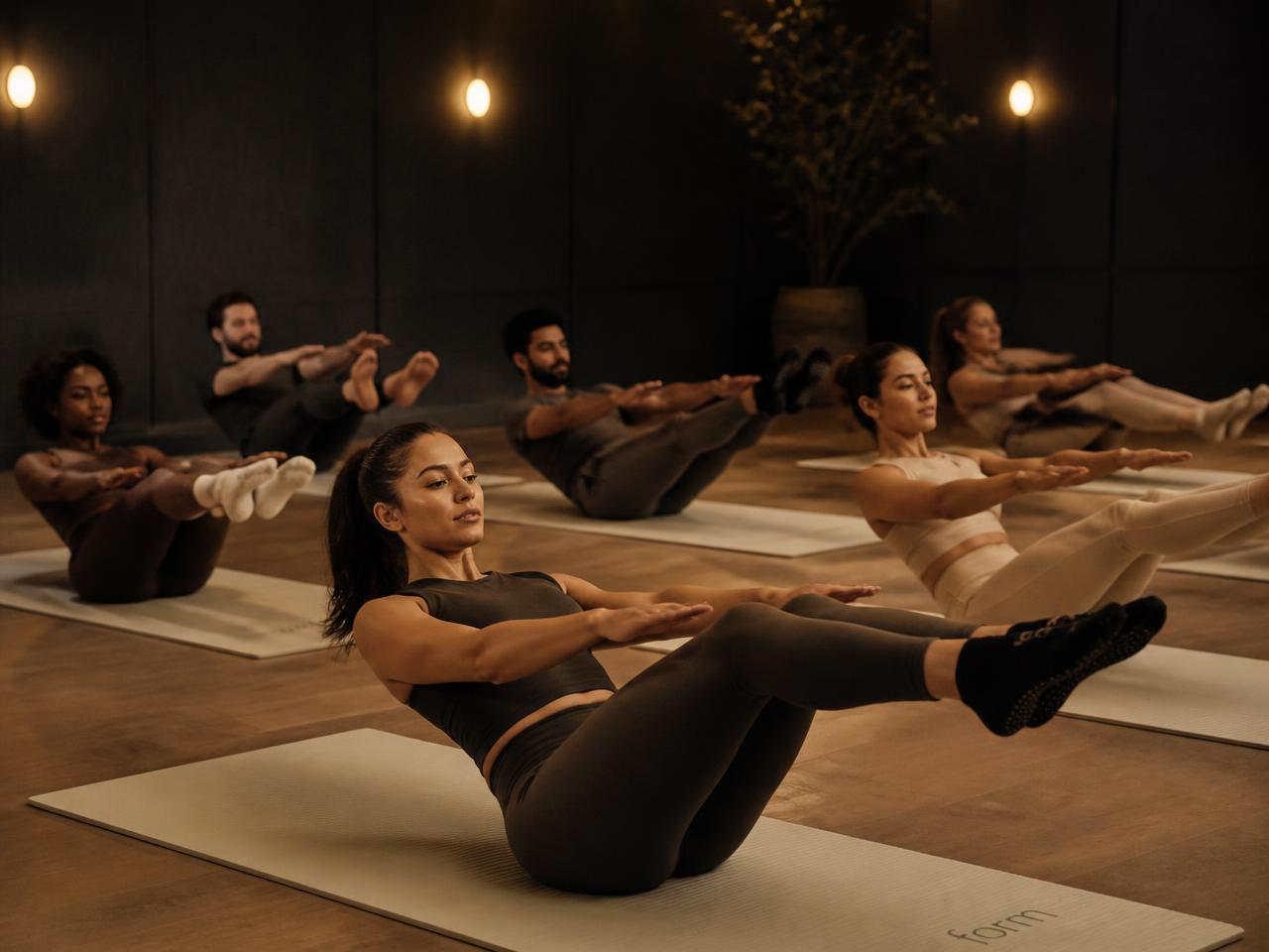 Members in a warmly lit boutique studio holding a controlled mat pilates core position